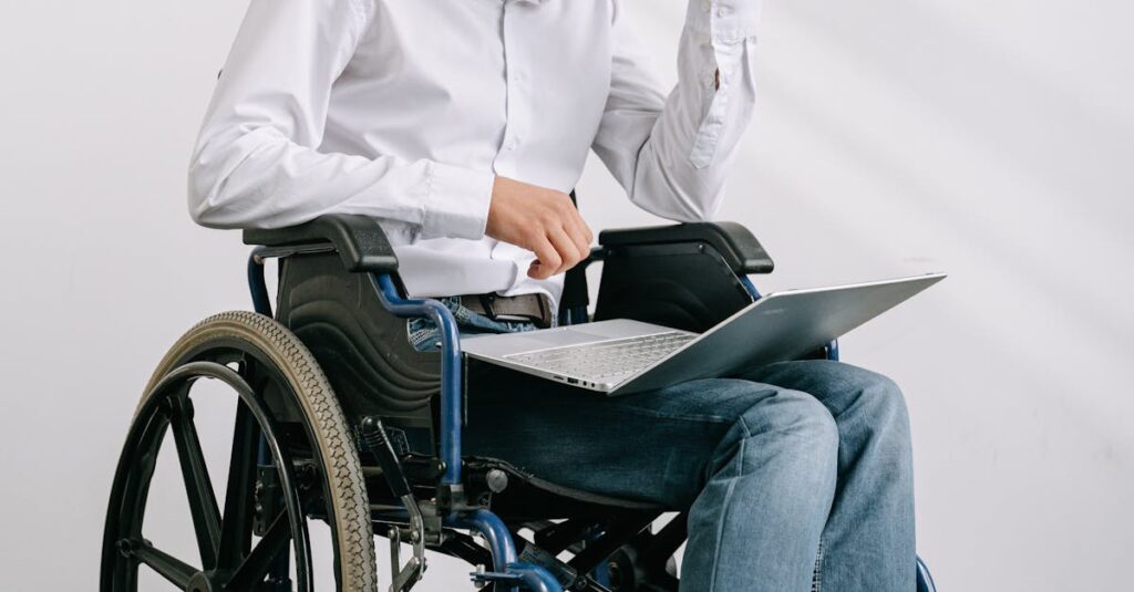 Man in wheelchair working on a laptop indoors, showcasing accessibility and technology.